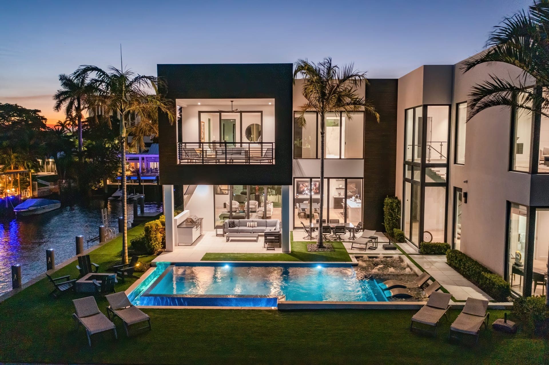 Twilight drone photography of a modern waterfront estate with warm interior glow