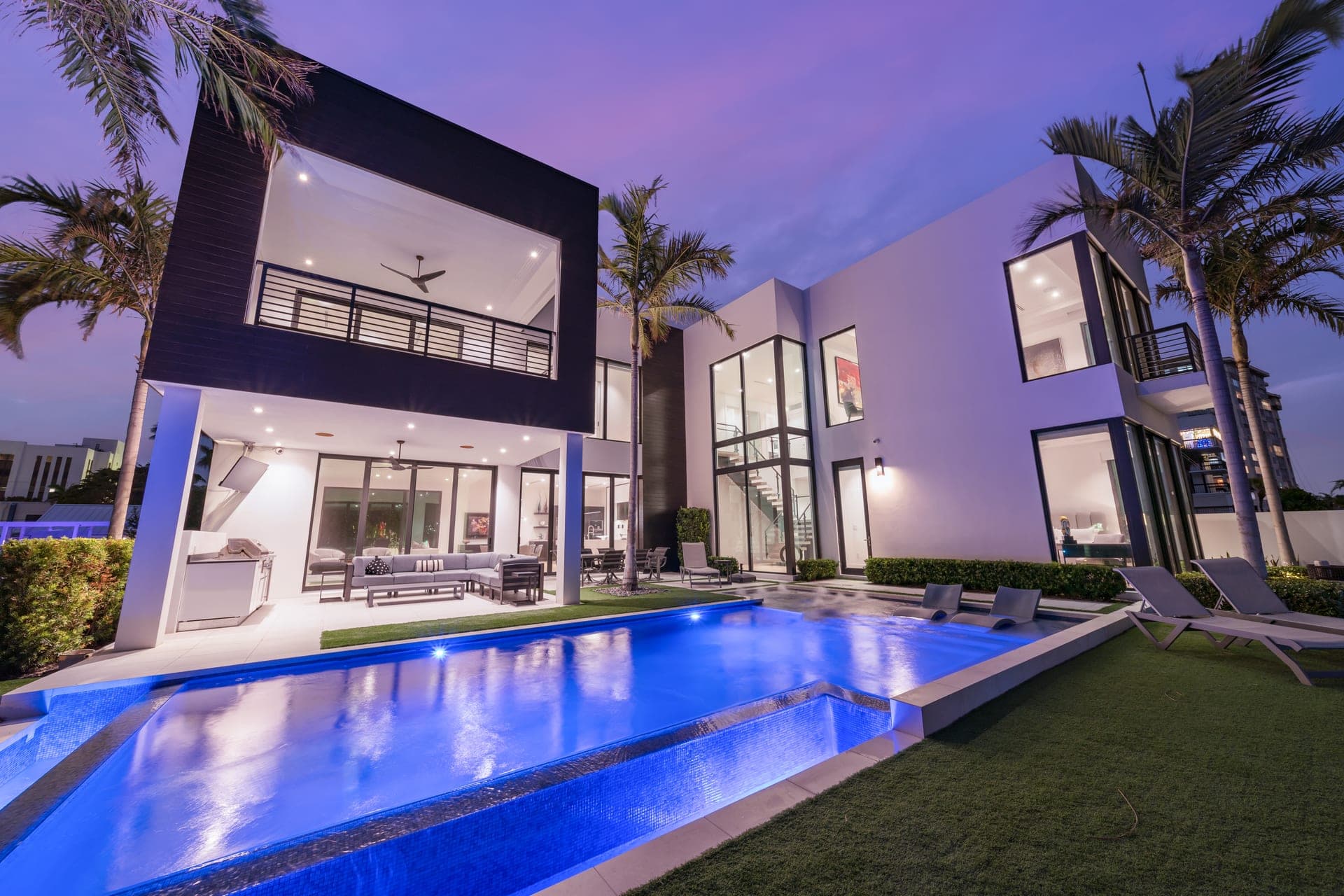 Wide-angle twilight view of an infinity pool stretching toward the modern estate's lit interior